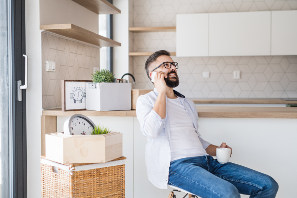 A mature man with coffee and smartphone moving in new home, making a phone call.