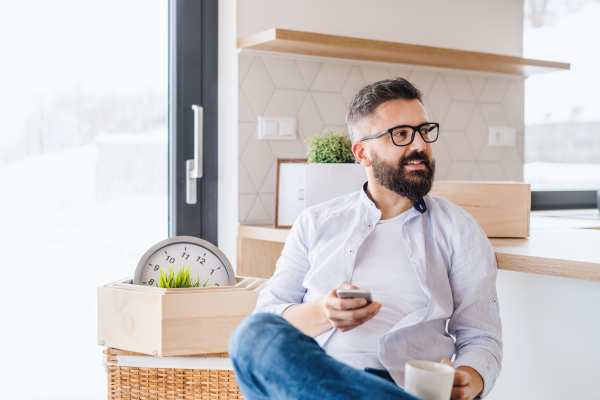 A mature man with coffee and smartphone moving in new home, text messaging.