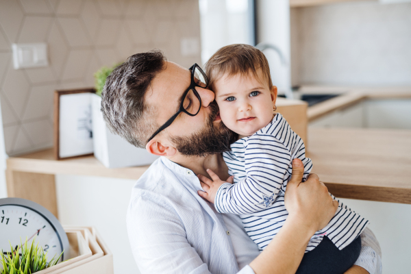 A close-up portrait of mature father with a toddler girl indoors, kissing.