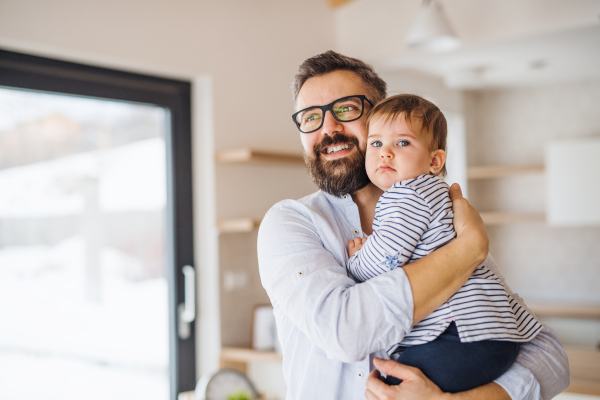 A portrait of mature father holding a toddler girl indoors, hugging.