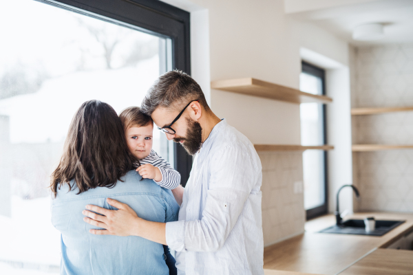 A young family with a toddler girl standing indoors at home. Copy space.