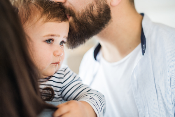 A midsection of young family with toddler girl standing indoors at home. A close-up.