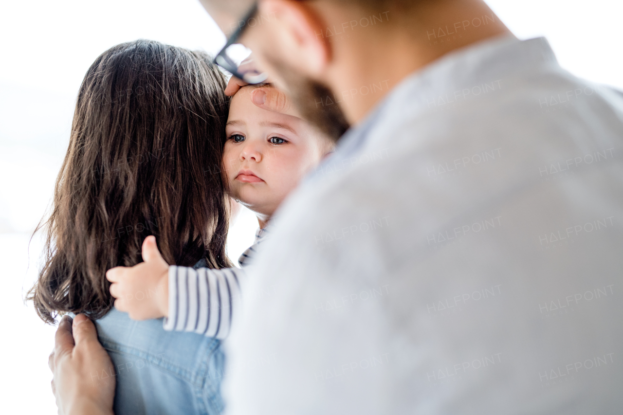 A young family with an unhappy crying toddler girl standing indoors at home.