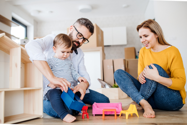 A portrait of happy young family with a toddler girl moving in new home, playing.