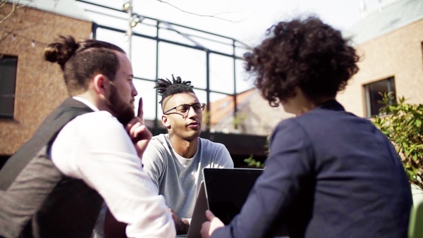 A group of young businesspeople using laptop in courtyard, start-up concept. Slow motion.