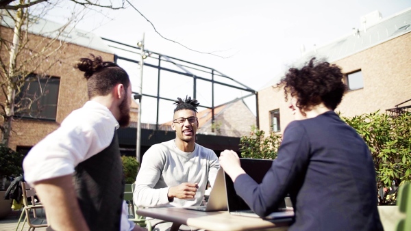 A group of young businesspeople using laptop in courtyard, start-up concept. Slow motion.