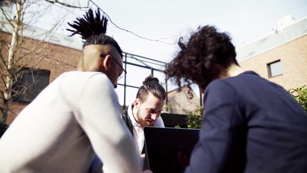 A group of young businesspeople using laptop in courtyard, start-up concept. Slow motion.