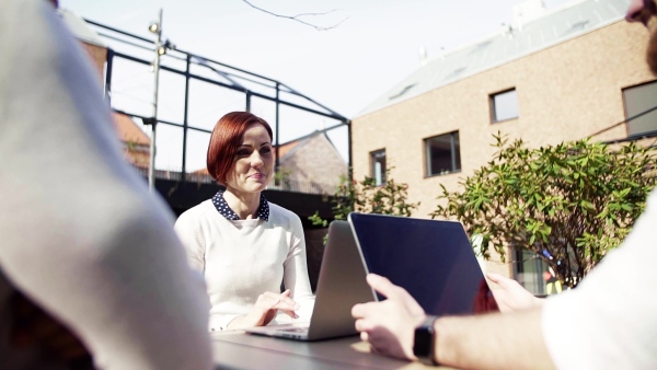 A group of young businesspeople using laptop in courtyard, start-up concept. Slow motion.