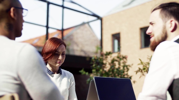 A group of young businesspeople using laptop in courtyard, start-up concept. Slow motion.