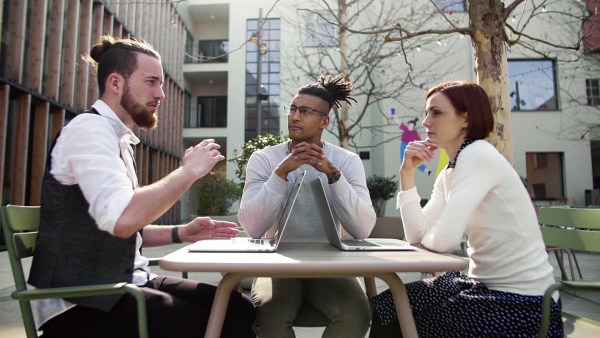 A group of young businesspeople using laptop in courtyard, start-up concept. Slow motion.