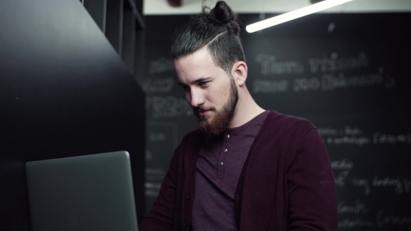 A young hipster businessman with laptop in office, working.