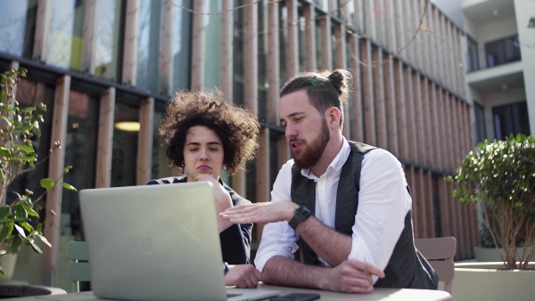 A group of young businesspeople using laptop in courtyard, start-up concept.