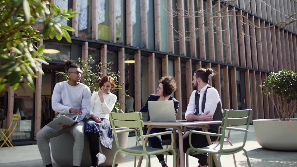 A group of young businesspeople using laptop in courtyard, start-up concept.