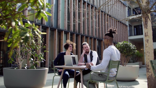 A group of young businesspeople with laptop in outdoor cafe, talking. A start-up concept.