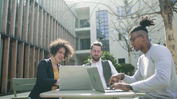 A group of young businesspeople using laptop in courtyard, start-up concept.