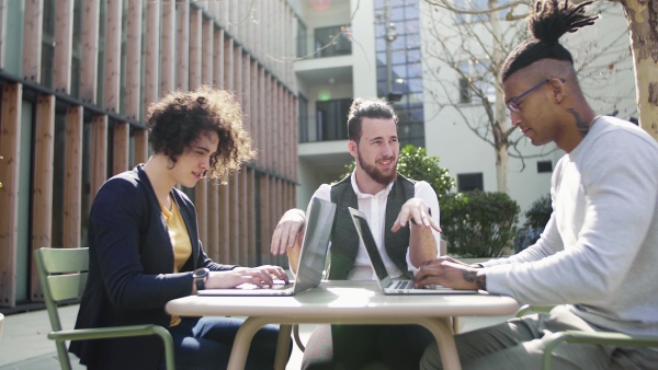 A group of young businesspeople using laptop in courtyard, start-up concept.