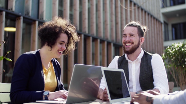 A group of young businesspeople using laptop in courtyard, start-up concept.