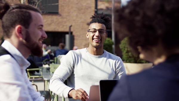 A group of young businesspeople using laptop in outdoor cafe, start-up concept.