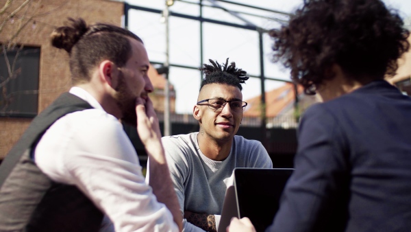 A group of young businesspeople with laptop in outdoor cafe, talking. A start-up concept.