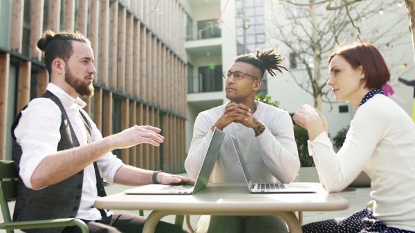 A group of young businesspeople using laptop in courtyard, start-up concept.