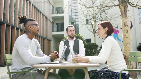 A group of young businesspeople using laptop in courtyard, start-up concept.