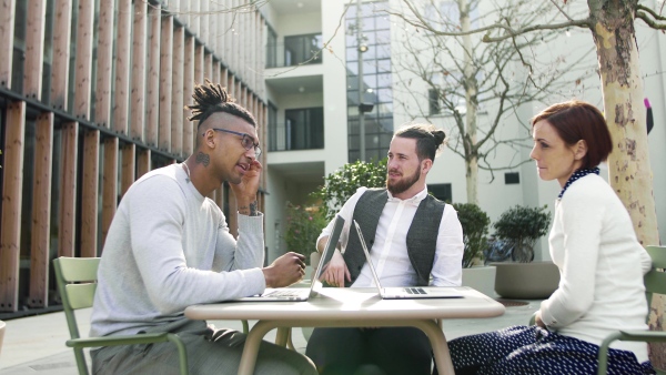 A group of young businesspeople using laptop in courtyard, start-up concept.