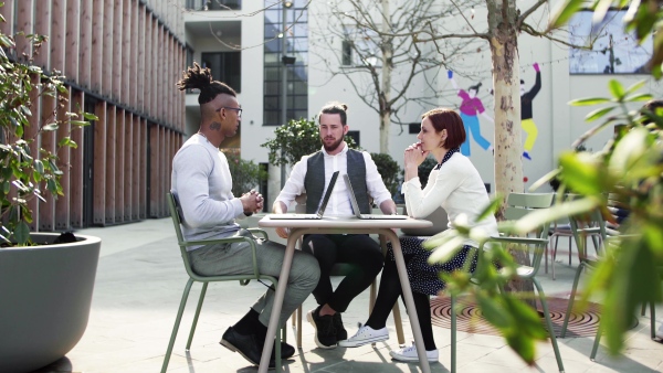 A group of young businesspeople using laptop in courtyard, start-up concept.