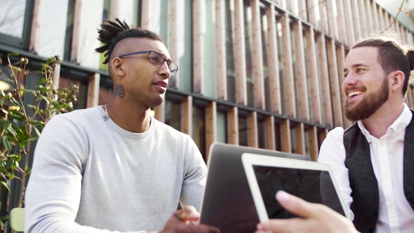 A group of young businesspeople with laptop in courtyard, talking. Start-up concept.