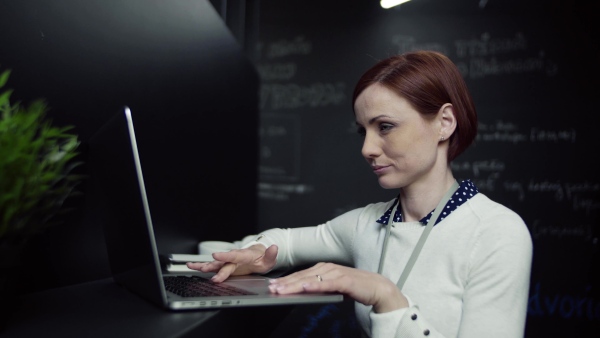 A young hipster businesswoman with laptop in office, working.