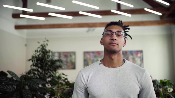 A portrait of young mixed race businessman with dreadlocks in office, looking at camera. Slow motion.