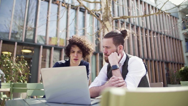 Two young businesspeople using laptop in courtyard, start-up concept. Slow motion.