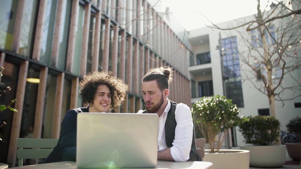 A group of young businesspeople using laptop in courtyard, start-up concept. Slow motion.