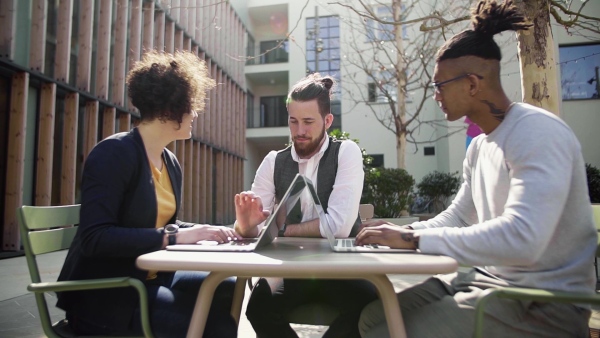 A group of young businesspeople using laptop in courtyard, start-up concept. Slow motion.