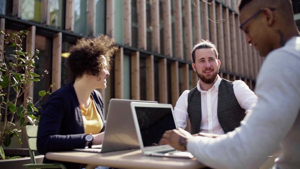 A group of young businesspeople using laptop in courtyard, start-up concept. Slow motion.