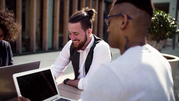 A group of young businesspeople with laptop in outdoor cafe, talking. A start-up concept. Slow motion.