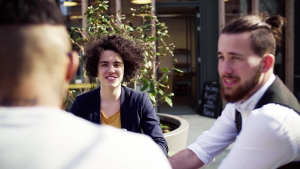 A group of young businesspeople with laptop in outdoor cafe, talking. A start-up concept. Slow motion.