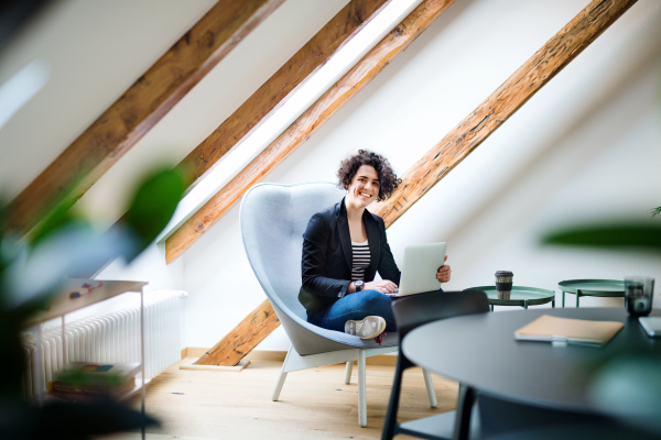 A young businesswoman with laptop sitting at the table in office, working.