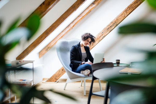 A young businesswoman with laptop sitting at the table in office, working.