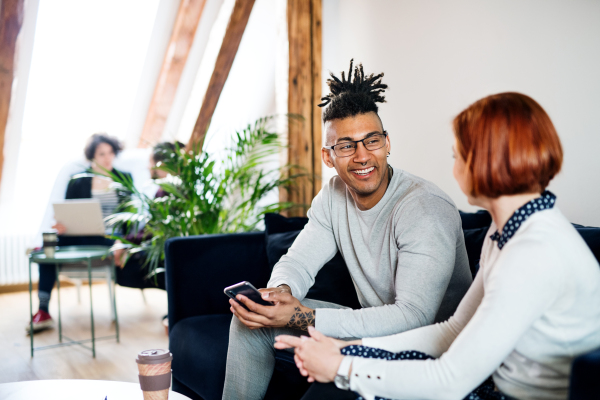 A group of young businesspeople with smartphone talking in office, start-up concept.