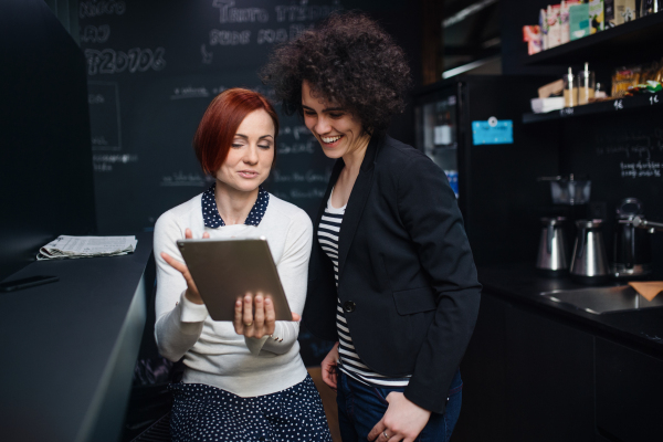 Two young cheerful female businesspeople using tablet in office, start-up concept.