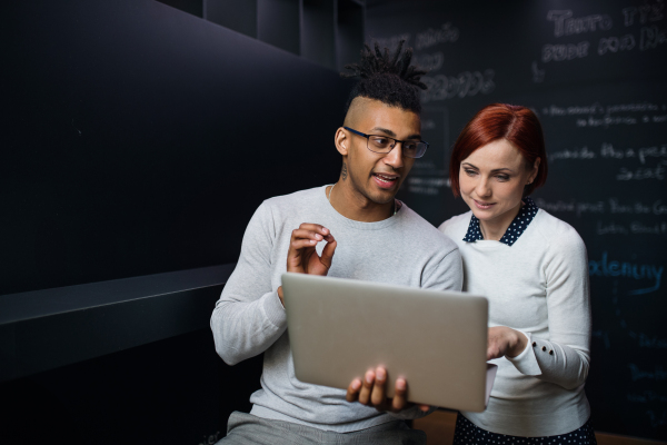 Two young cheerful businesspeople using laptop in office, start-up concept.