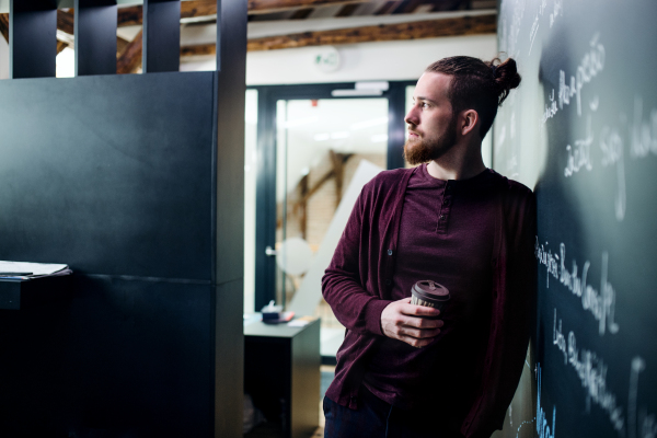 A young businessman with coffee in office, having a break.