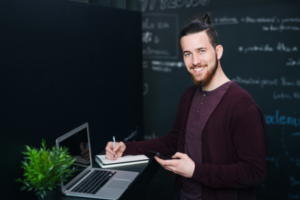 Young businessman with laptop and smartphone in office, working.