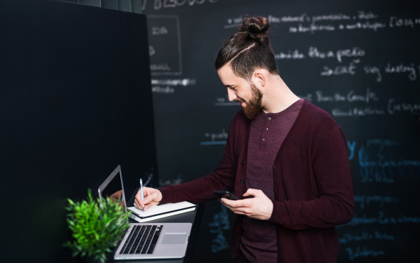 Young businessman with laptop and smartphone in office, working.