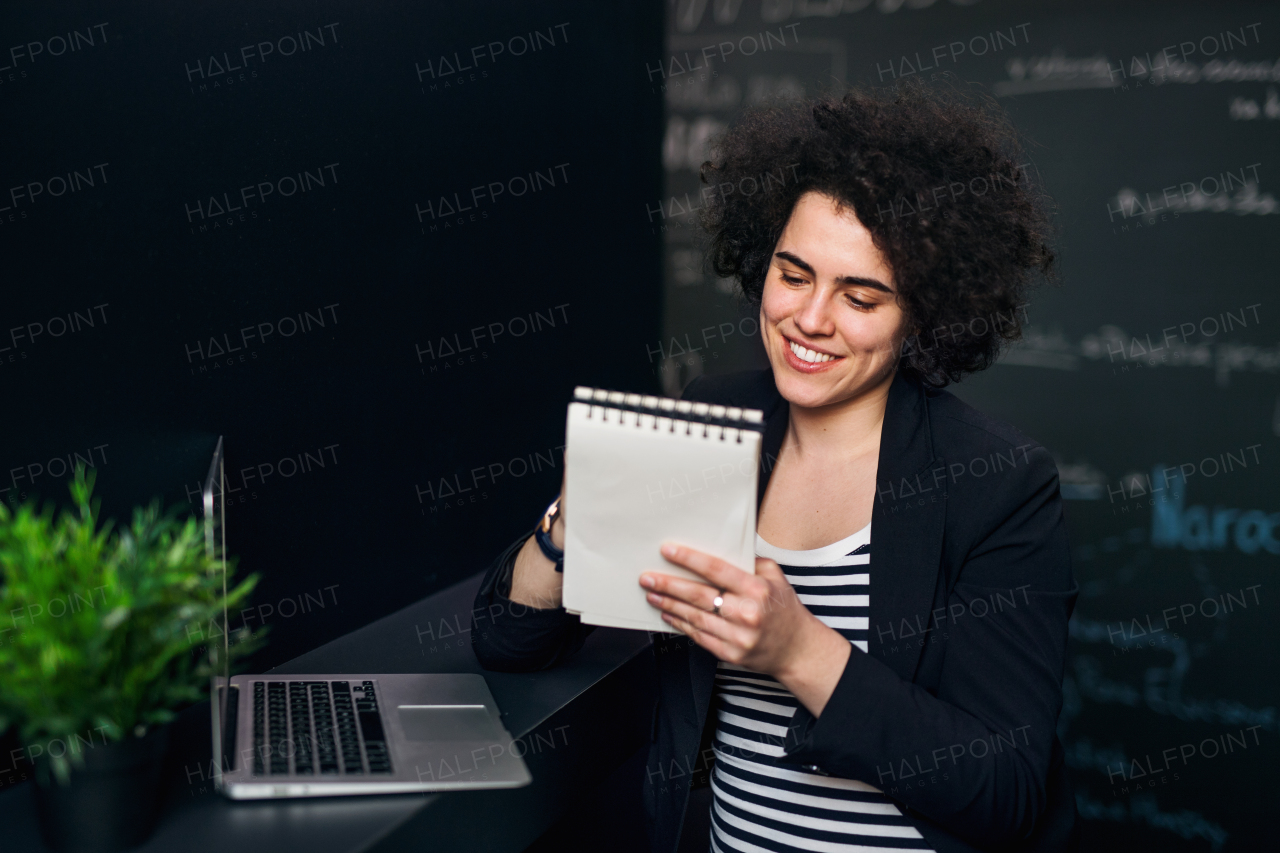 A young businesswoman with laptop in office, writing when working.