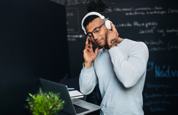 A young businessman with headphones in office, listening to music.