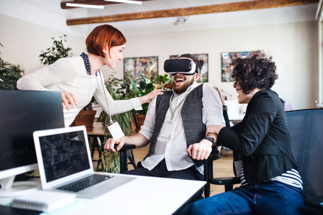 A group of young businesspeople with VR goggles talking in office, start-up concept.