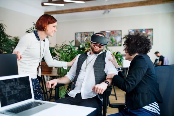 A group of young businesspeople with VR goggles talking in office, start-up concept.