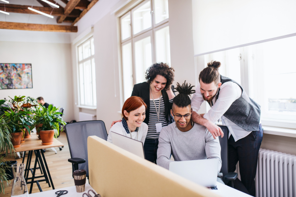 A group of young cheerful businesspeople using laptop in office, start-up concept.