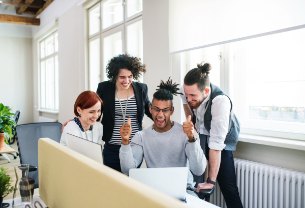 A group of young cheerful businesspeople using laptop in office, start-up concept.